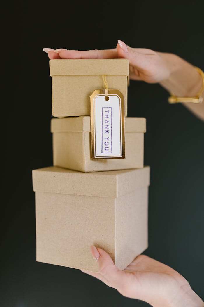 contact-img Three kraft gift boxes stacked with a 'Thank You' tag held by a woman's hands.